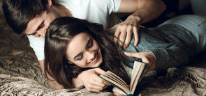 Happy couple lying on bed together while reading a book, illustrating intimacy and connection for BJ techniques.
